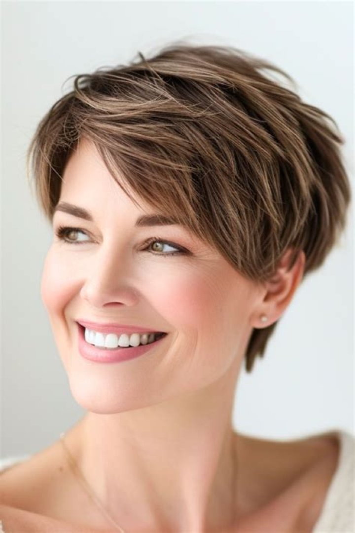 a woman with short hair standing in front of a white wall wearing a